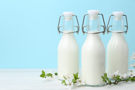 Fresh milk and blossoms on white table against light blue background. Space for textの写真素材