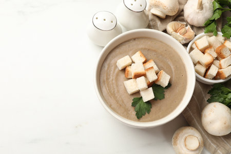 Delicious mushroom cream soup with croutons, parsley and ingredients on white table, flat lay. Space for textの写真素材