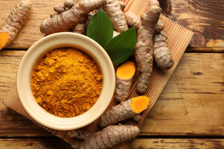 Turmeric powder in bowl, roots and leaves on wooden table, flat layの写真素材