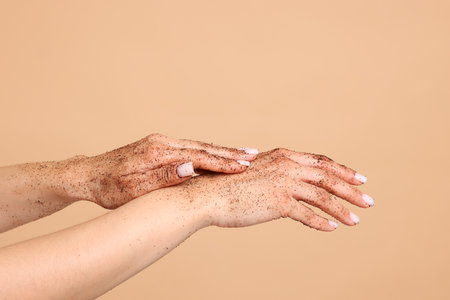 Woman applying body scrub onto her hands on beige background, closeupの写真素材