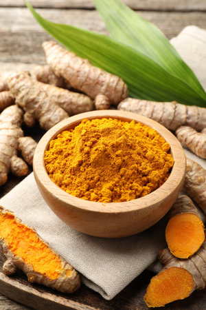 Turmeric powder in bowl, roots and leaves on table, closeupの写真素材