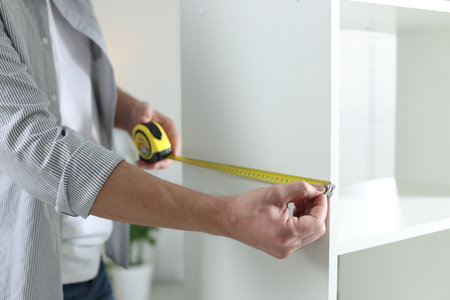 Man measuring white shelving unit with tape indoors, closeupの写真素材