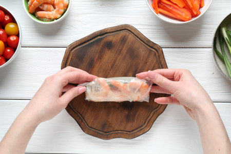 Woman making tasty spring roll at white wooden table, top viewの写真素材