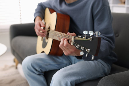 Young man playing guitar on sofa indoors, closeup