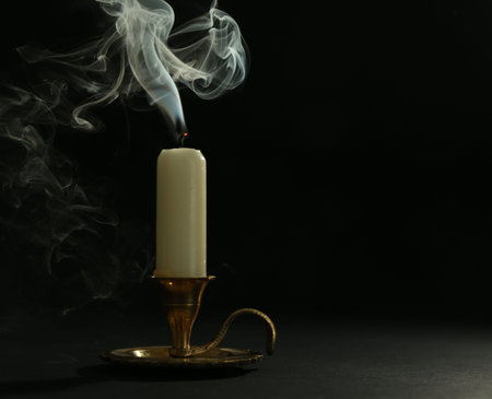 Extinguished candle in candlestick on black background, space for textの写真素材