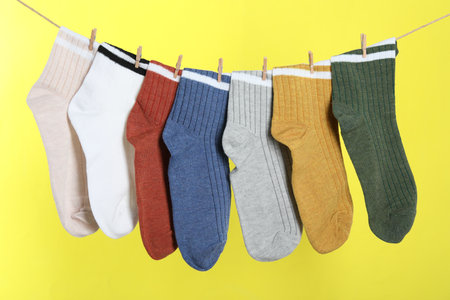 Different socks hanging on washing line against yellow backgroundの写真素材