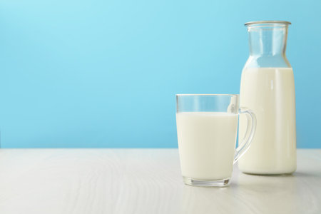 Fresh milk in cup and jug on white wooden table against light blue background. Space for textの写真素材