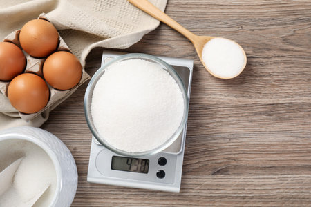 Digital kitchen scale with bowl of sugar and eggs on wooden table, flat layの写真素材