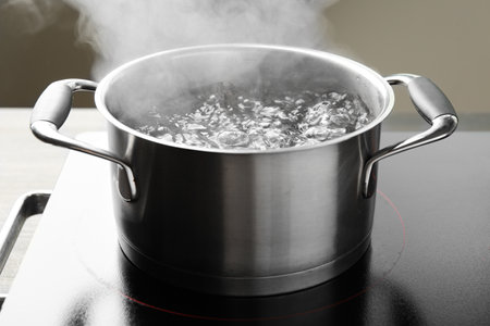 Cooking pot with boiling water and stove on table against gray background, closeupの写真素材