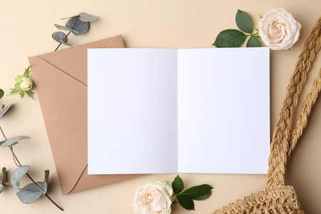 Blank greeting card, envelope, roses, bag and eucalyptus leaves on beige background, flat lay