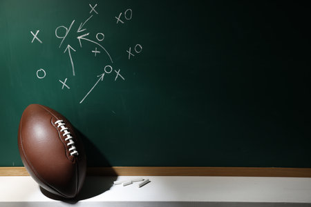 American football ball and pieces of chalk near chalkboard with game scheme, space for textの写真素材