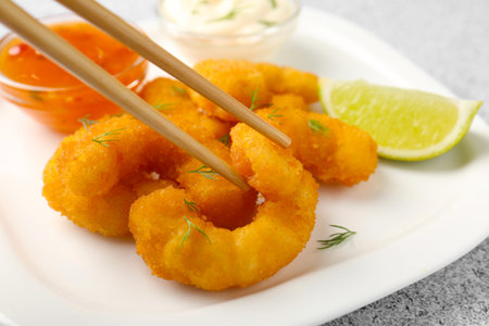 Taking tasty tempura shrimp with chopsticks from plate at gray textured table, closeup