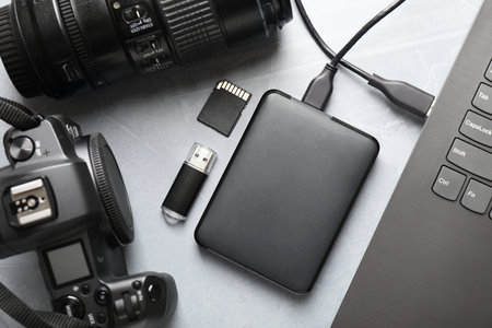 External hard disk connected to laptop, SD memory card, flash drive, camera and lens on gray...
