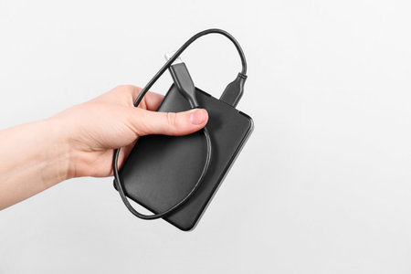Man holding external hard drive with USB cable on light grey background, closeup. Space for textの写真素材
