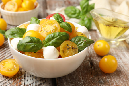 Fresh salad with yellow tomatoes, basil and mozzarella cheese on wooden table, closeupの写真素材