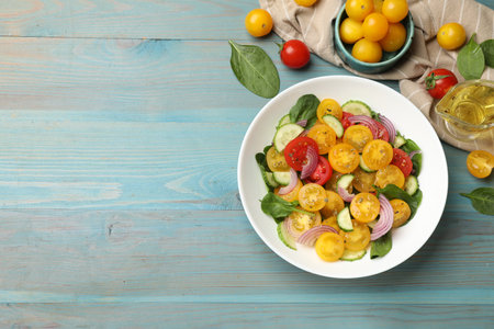 Fresh salad with yellow tomatoes served on light blue wooden table, flat lay. Space for textの写真素材