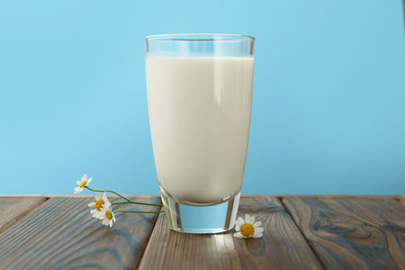 Fresh milk in glass and flowers on wooden table against light blue background, closeupの写真素材