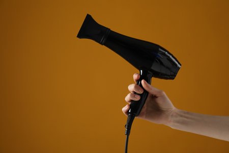 Woman with hair dryer on orange background, closeup. Space for textの写真素材