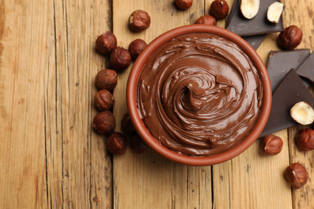 Tasty hazelnut spread, chocolate pieces and nuts on wooden table, flat lay. Space for text