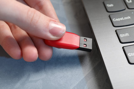 Woman inserting flash drive into laptop at gray textured table, closeup