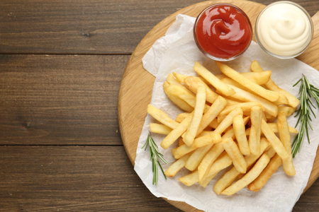 Tasty French fries with sauces and rosemary on wooden table, top view. Space for text