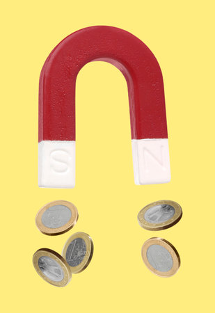 Horseshoe magnet attracting coins on yellow backgroundの写真素材