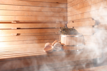 Bucket, whisk, ladle and towels on wooden bench surrounded by steam in sauna