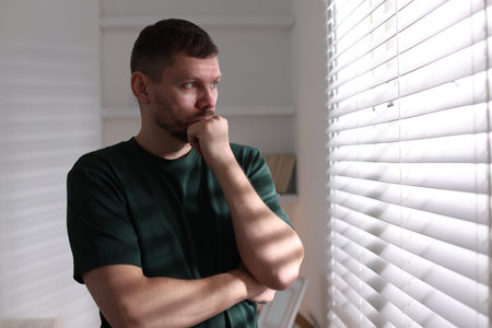 Depressed man looking out window at home