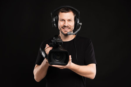 Man with professional video camera and headset on black background