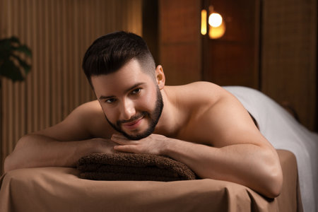 Handsome man lying on massage table in spa salonの写真素材