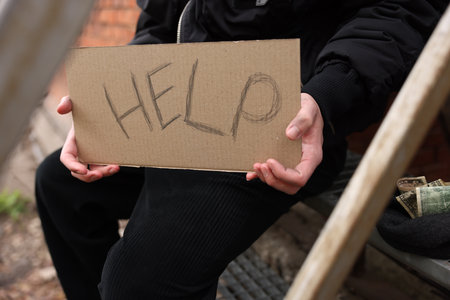 Homeless man holding sign with word Help outdoors, closeupの写真素材