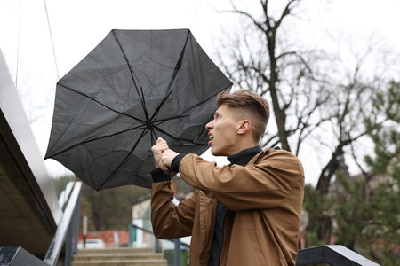 Man with broken umbrella fighting wind under rain outdoorsの写真素材