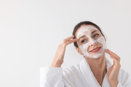 Spa day. Beautiful woman applying mask onto her face on white background, space for textの写真素材