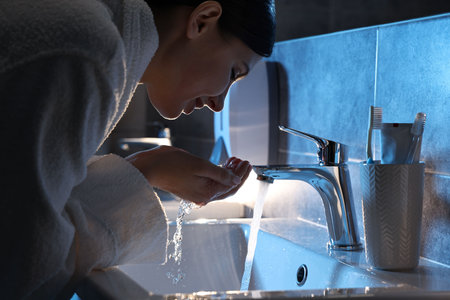 Woman washing her face over sink in bathroomの写真素材