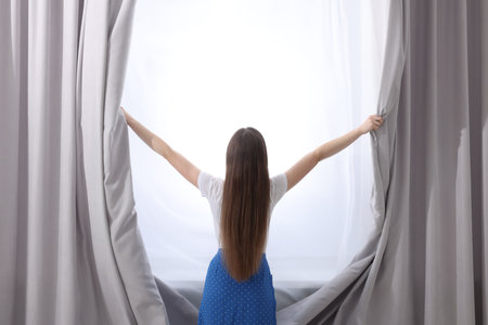 Woman opening stylish curtains at home, back viewの写真素材