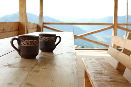 Two cups of hot drink on wooden table near mountainsの写真素材
