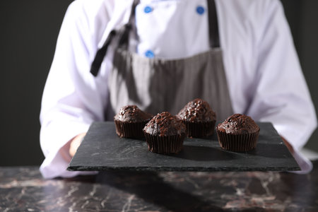Confectioner with tasty chocolate muffins at dark table, closeupの写真素材
