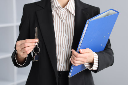 Real estate agent holding key with house shaped keychain and folder indoors, closeupの写真素材