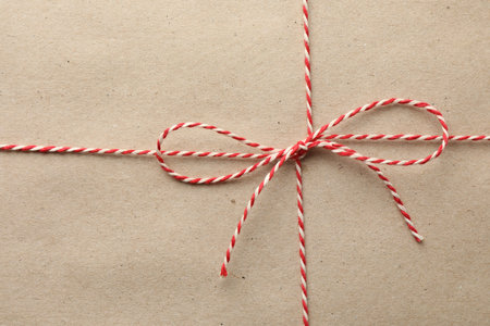Gift wrapped in kraft paper and bow as background, top view