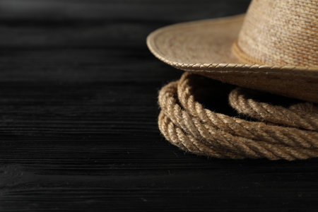 Cotton rope and straw hat on black wooden background, closeup. Space for textの写真素材