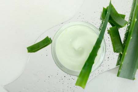 Moisturizing cream with extract of aloe vera, cut leaves and wet mirror on white background, flat layの写真素材