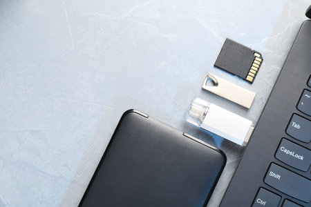 Flash drives, SD memory card, external hard disk and laptop on gray textured table, flat lay. Space for textの写真素材