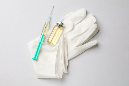 Hepatitis vaccine in glass vial, syringe and medical gloves on grey background, top viewの写真素材