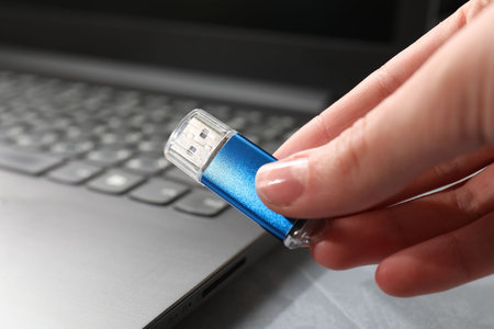 Woman with flash drive and laptop at gray table, closeup
