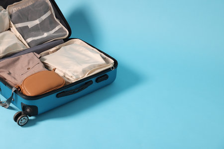 Suitcase with clothes, bag and other belongings on light blue background, space for textの写真素材