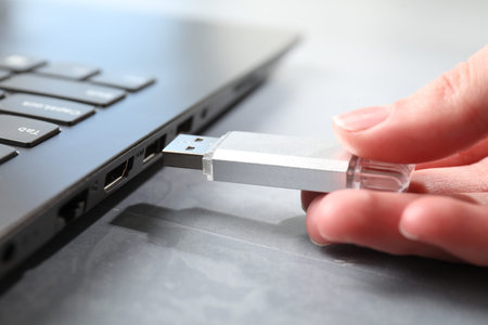 Woman inserting flash drive into laptop at gray textured table, closeup