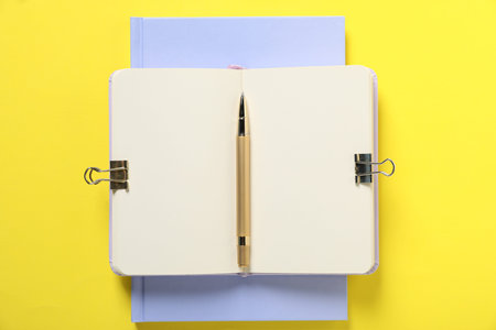 Pen and notebooks on yellow background, top view