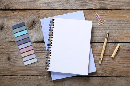 Pen, notebooks, paper clips and colorful stickers on wooden table, flat lay