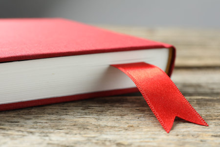 Book with red ribbon bookmark on wooden table against grey background, closeup