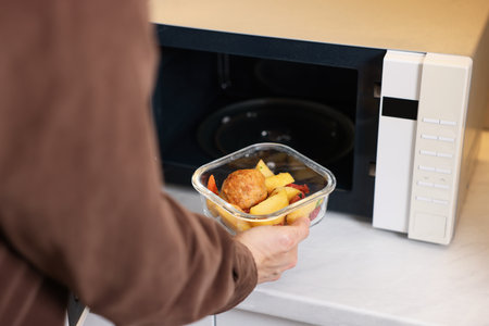 Man putting container with lunch into microwave in kitchen, closeupの写真素材